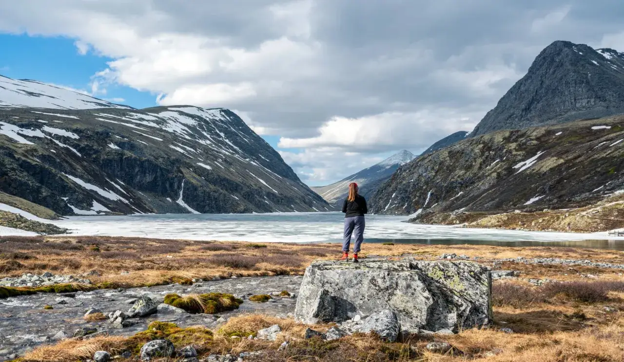 En person st&aring;r vid en frusen sj&ouml; i en norsk dalg&aring;ng, omgiven av sn&ouml;kl&auml;dda berg. En vacker vy som p&aring;minner om en triangeltur i Norge.