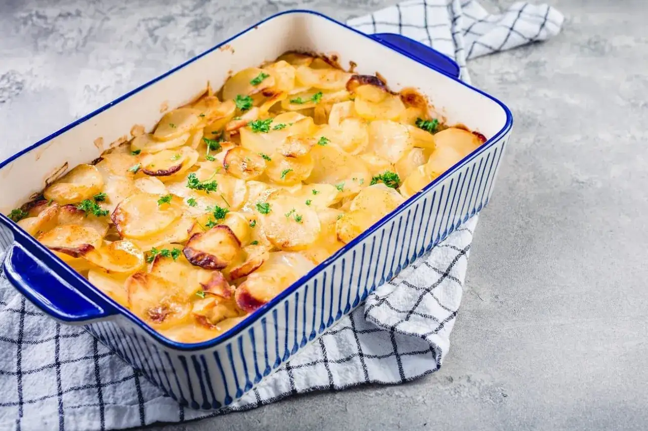 Ein goldbrauner Kartoffelauflauf, garniert mit Petersilie, in einer blauen Keramikform. Perfekt f&uuml;r Ihre Auflauf Rezepte.