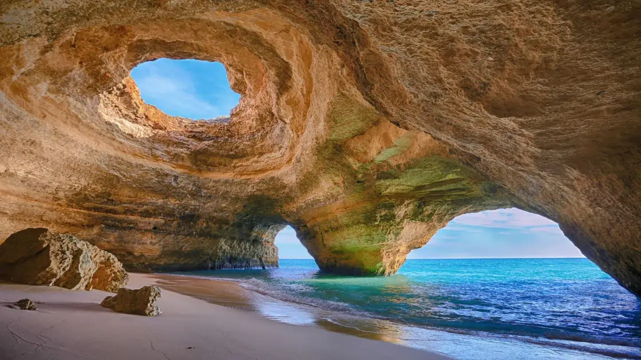 Gruta marina con arena dorada y mar turquesa, ideal para tu plan de algarve en 6 d&iacute;as.