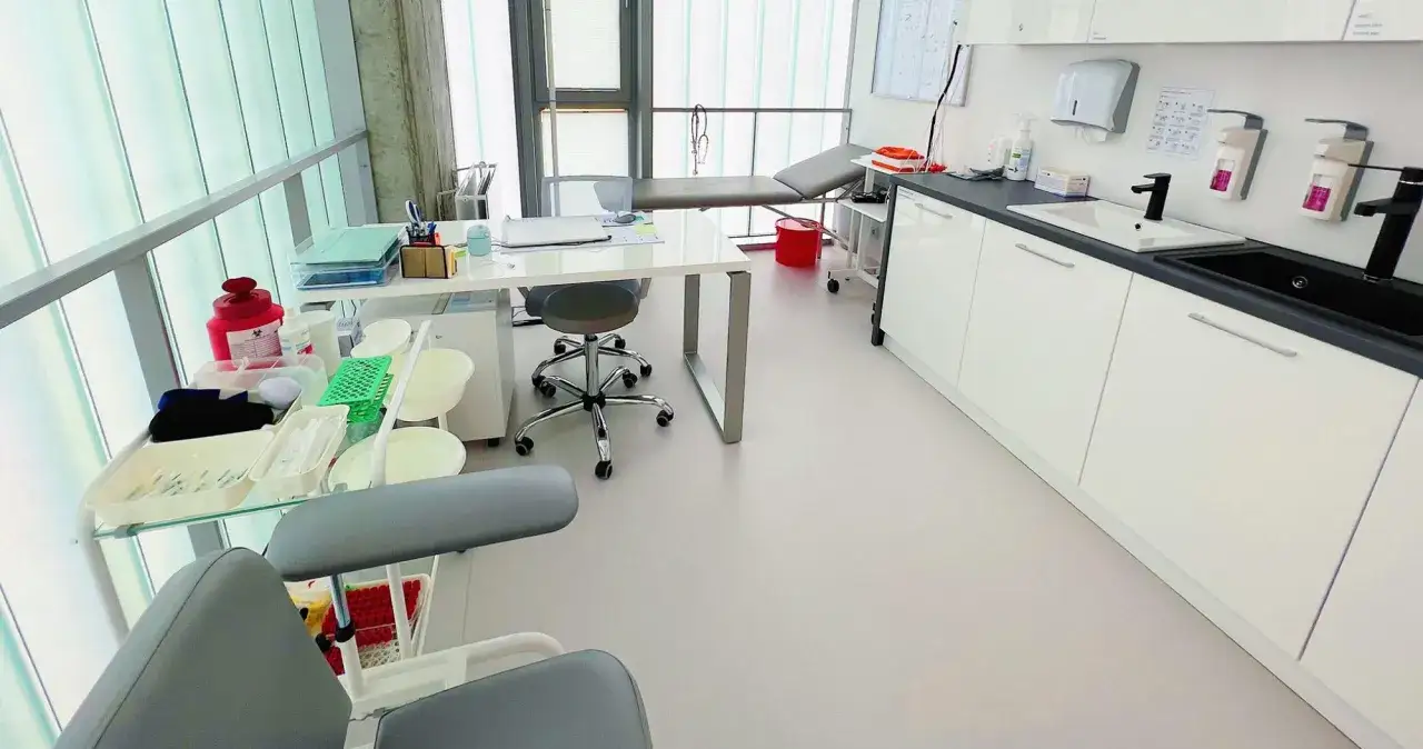 Gabinet zabiegowy z kozetką, biurkiem i wózkiem z materiałami do pobierania krwi na czczo.