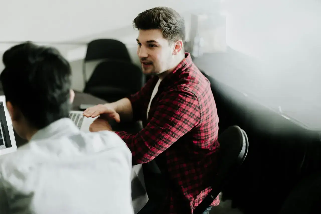 Dwóch mężczyzn przy laptopie omawia strategię, jak znaleźć inwestora do biznesu. Jeden z nich gestykuluje, tłumacząc pomysł.