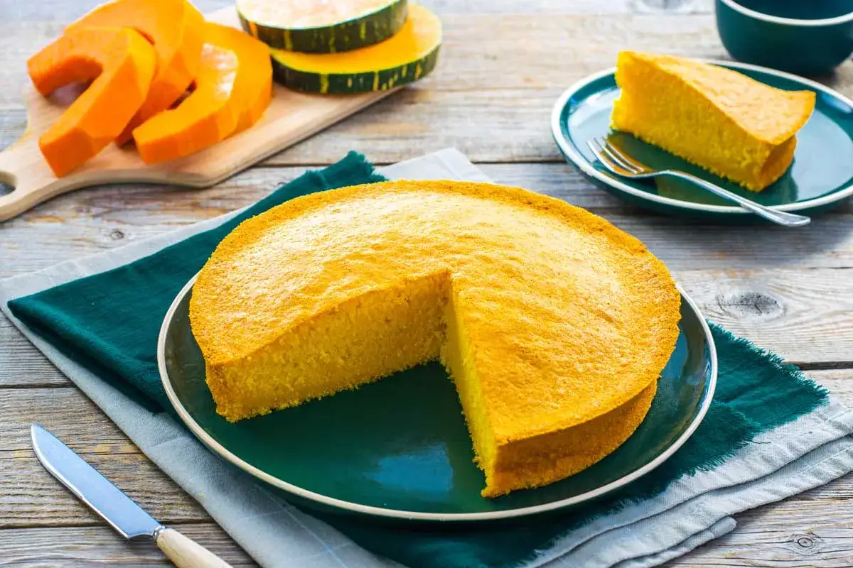 Una torta di zucca dorata, soffice e invitante, con spicchi di zucca fresca e fette già pronte per essere gustate.