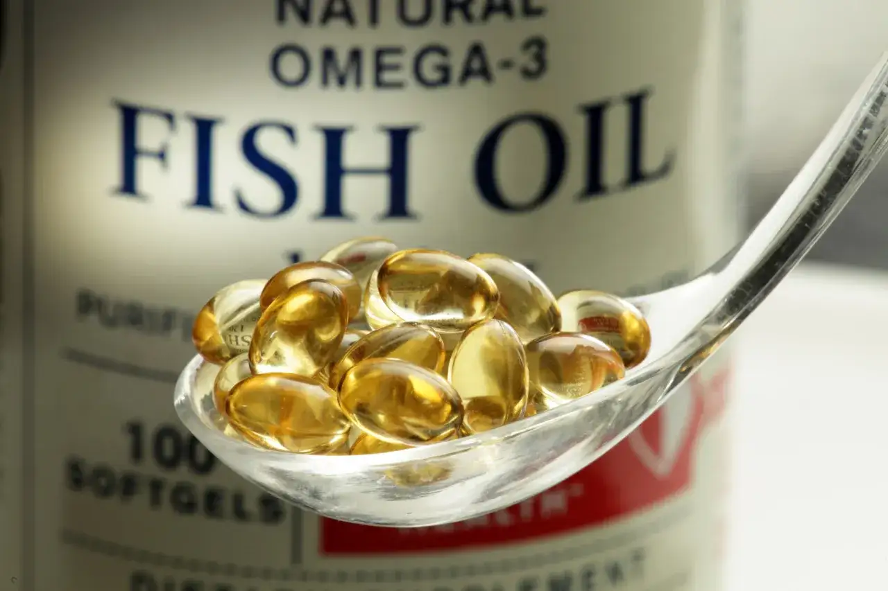 Łyżeczka pełna kapsułek z olejem rybim, kluczowych dla suplementacji omega 3. W tle etykieta