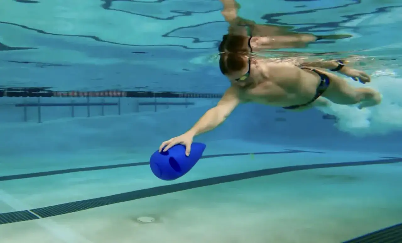 Swimmer underwater, reaching for a blue kickboard swim aid.