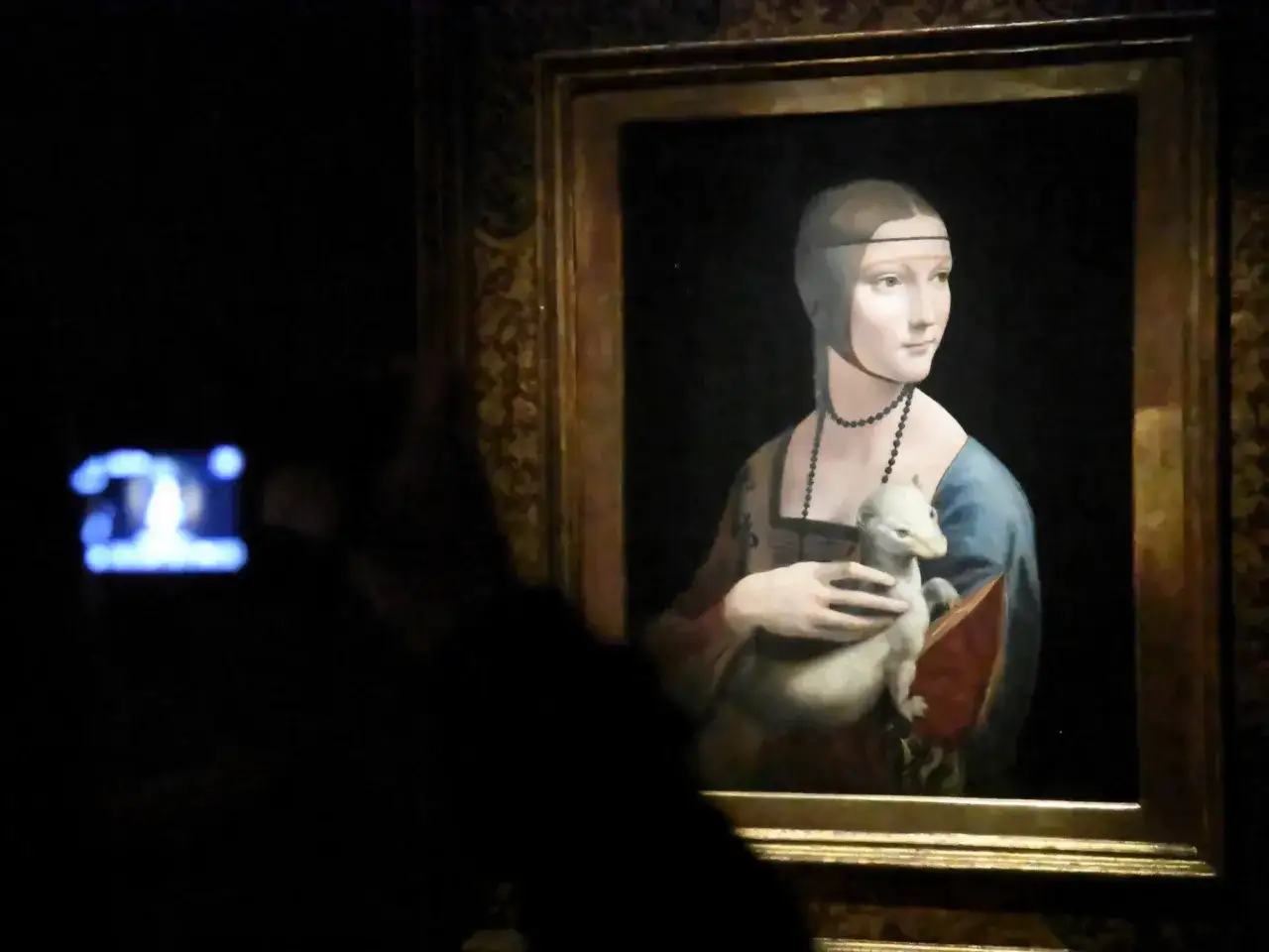 Dama z łasiczką, obraz Leonarda da Vinci, w złotej ramie. W ciemnościach widać zarys osoby fotografującej dzieło.