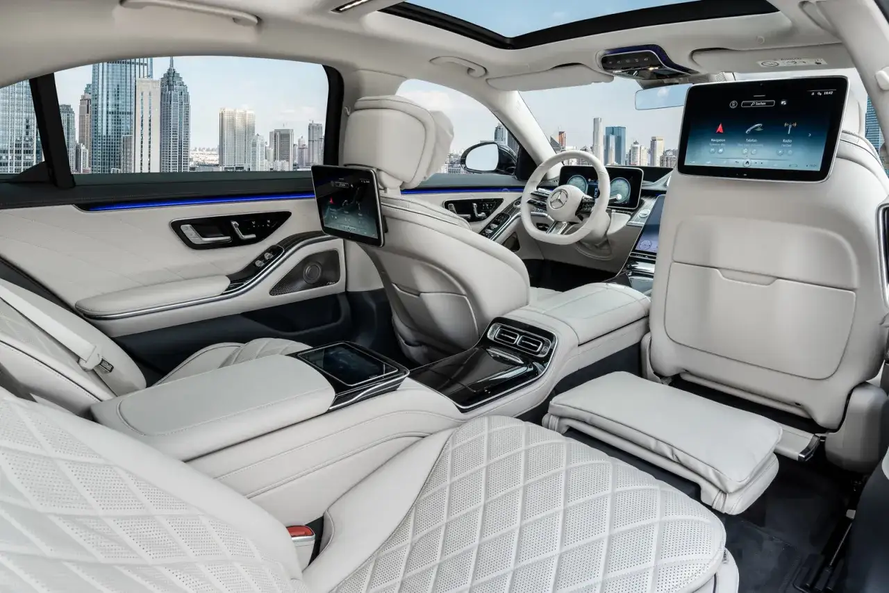Luksusowe wnętrze Mercedes S500 z białej skóry, ekranami dla pasażerów i widokiem na miasto.