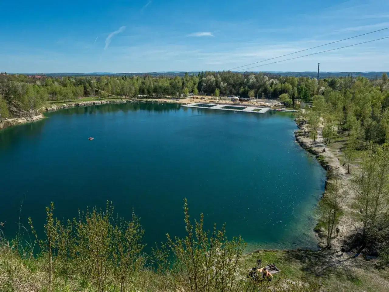 Turkusowe jezioro, plaża i kąpieliska tworzą polski Balaton. W oddali las i błękitne niebo.