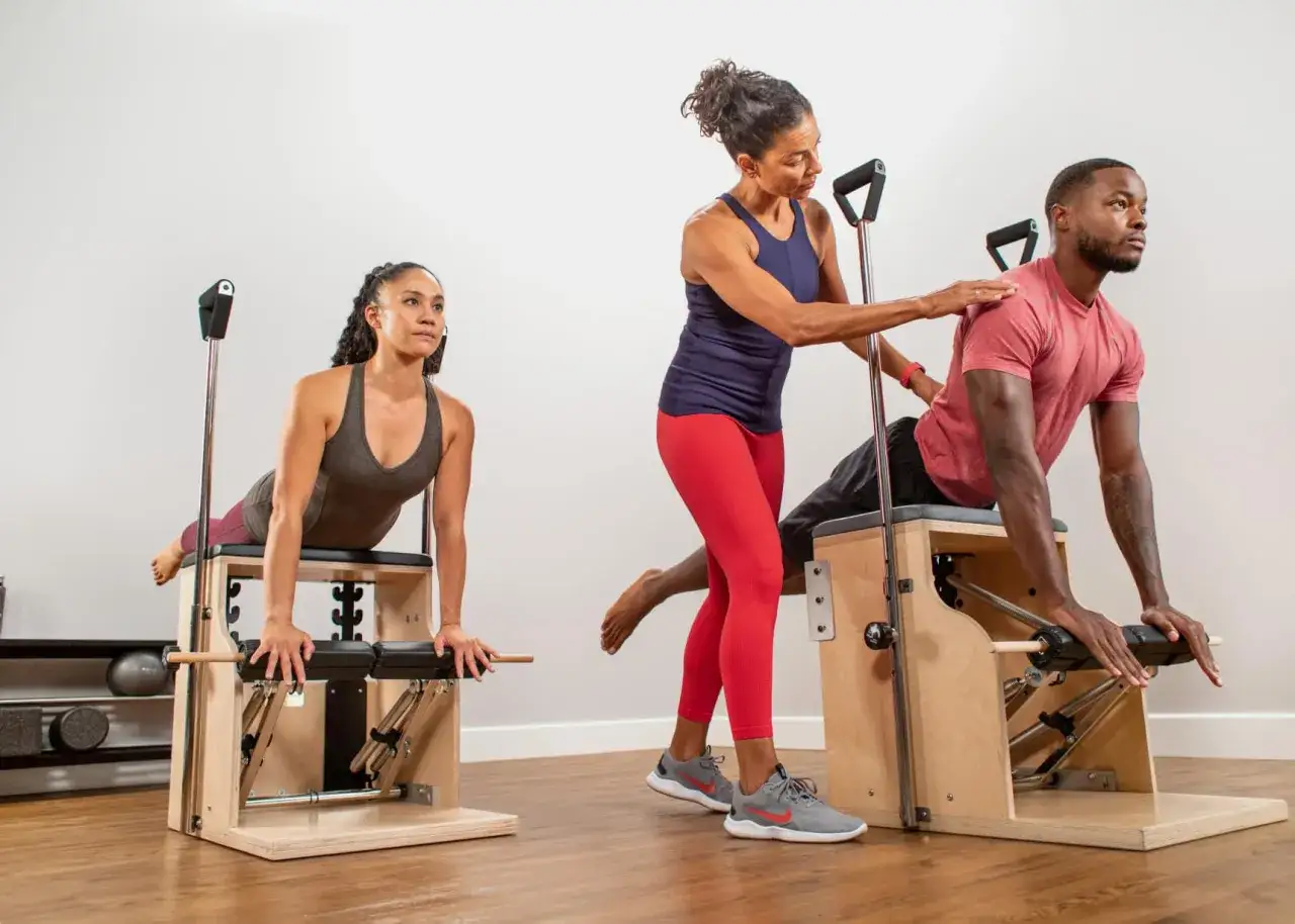 Instructor gu&iacute;a a dos personas en diferentes tipos de pilates en m&aacute;quinas.