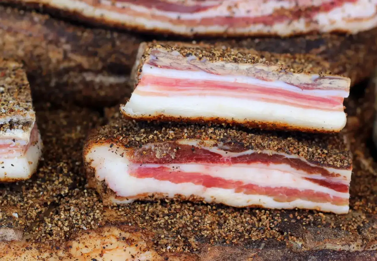 Stapel von italienischem Speck, mit Schichten aus weißem Fett und rosa Fleisch, bedeckt mit grobem Pfeffer.