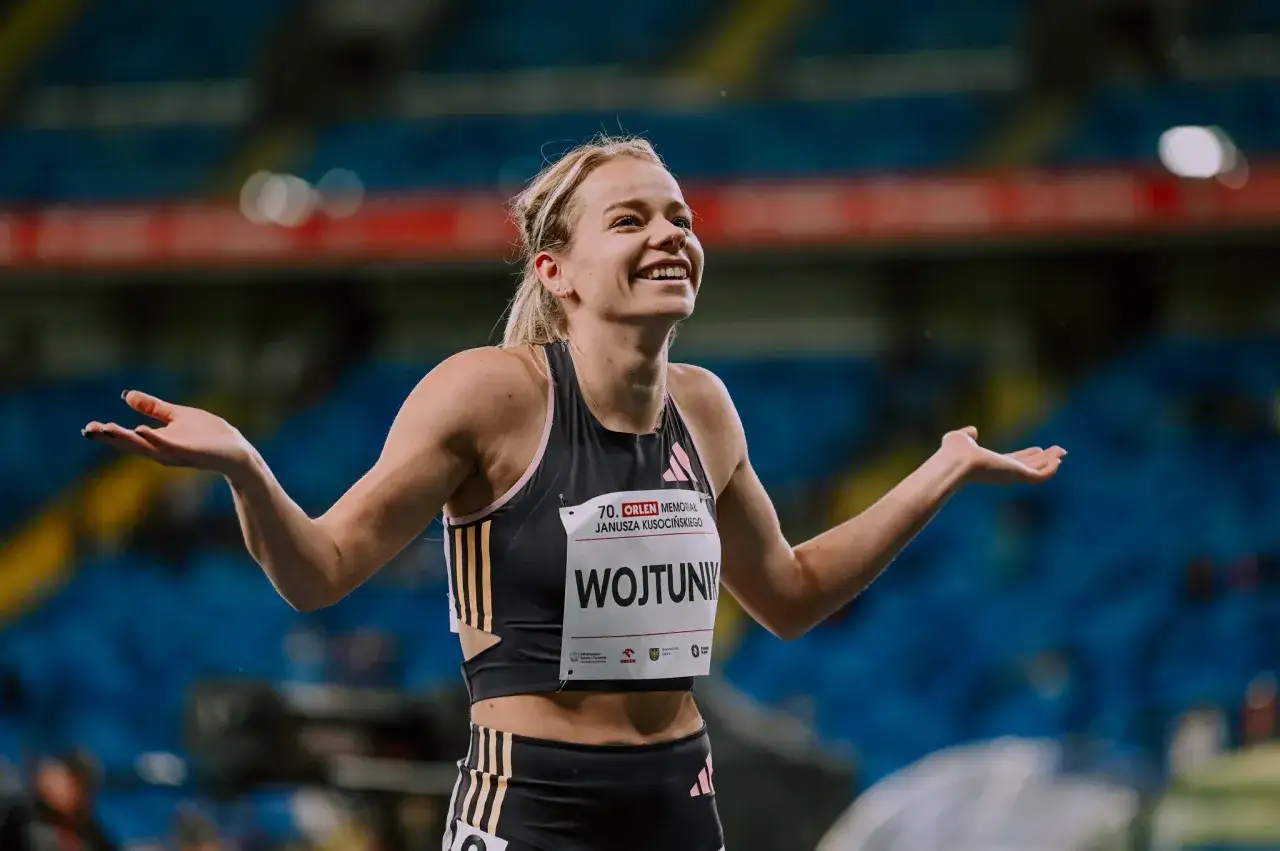 Uśmiechnięta Klaudia Wojtunik, lekkoatletka, cieszy się po biegu, rozkładając ręce.