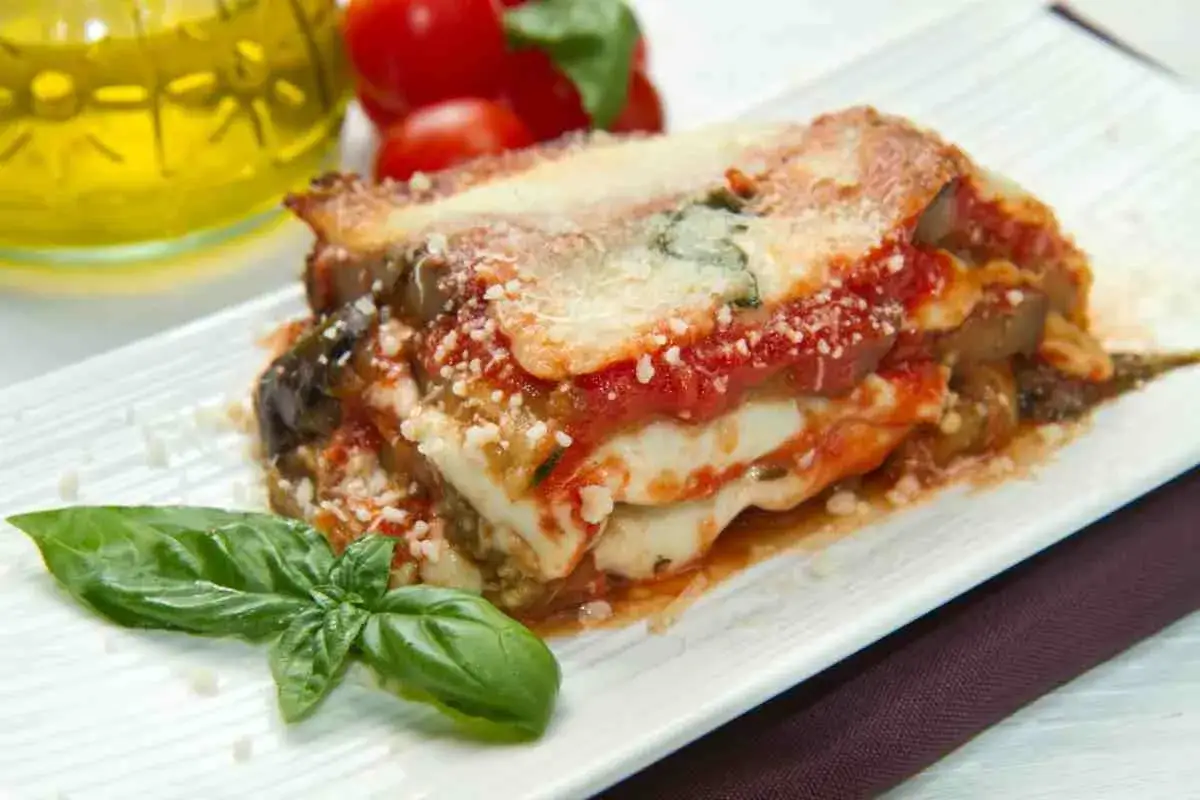 Una fetta di parmigiana di mare pugliese, ricca di melanzane, pomodoro e mozzarella filante, guarnita con basilico fresco.