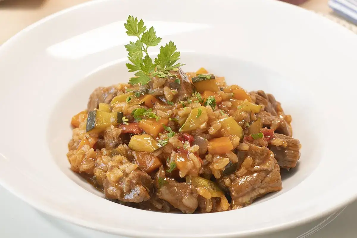 Un plato de arroz con carne, jugoso y lleno de verduras como calabac&iacute;n y zanahoria, adornado con perejil fresco.