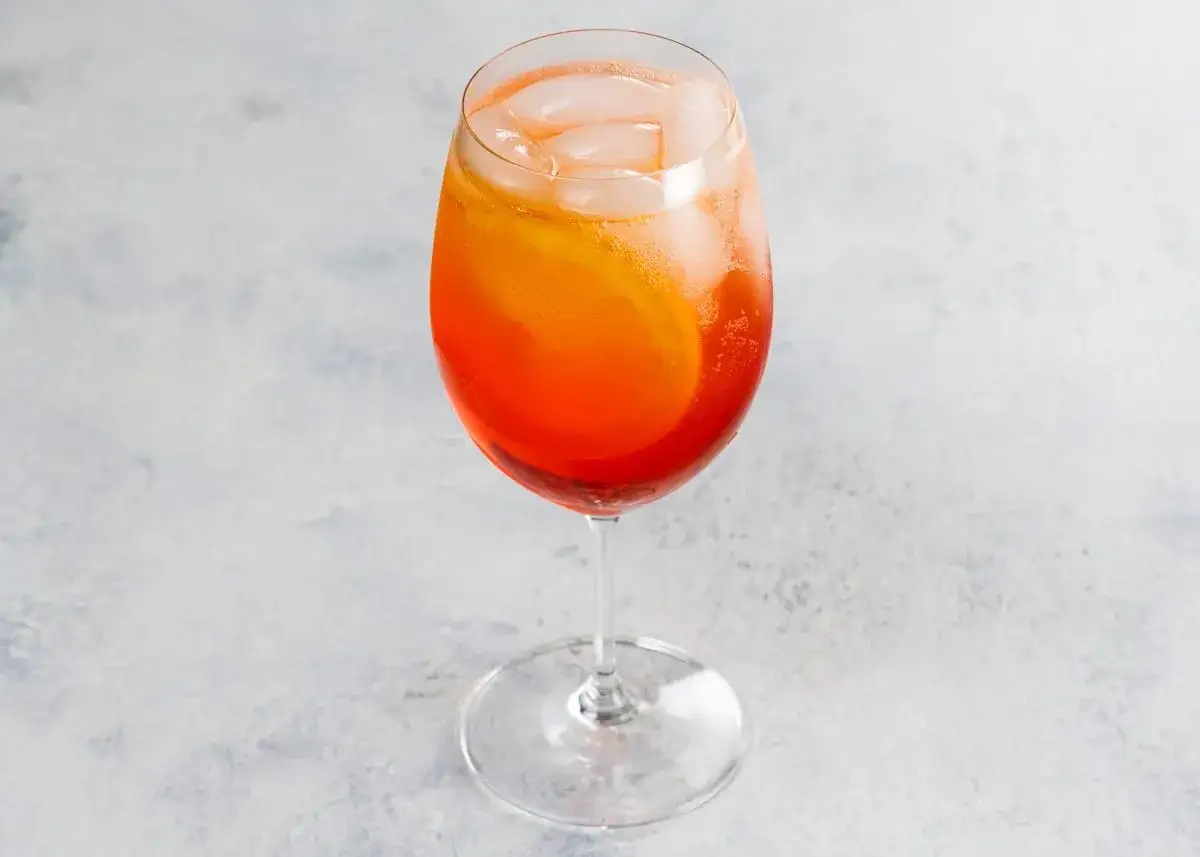 Un verre de cocktail Aperol Spritz, rempli de gla&ccedil;ons et d'une tranche d'orange. La recette parfaite pour un ap&eacute;ritif rafra&icirc;chissant.
