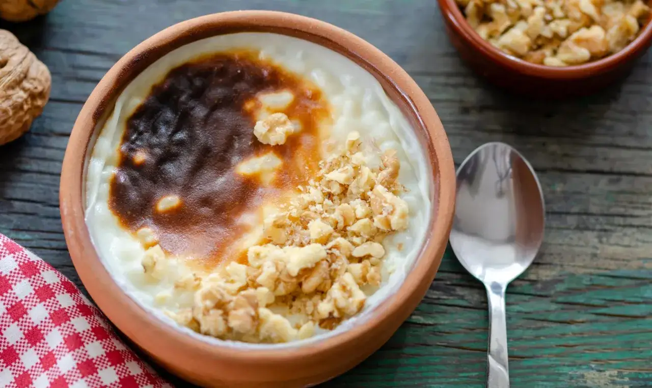 Un délicieux riz au lait au four, gratiné et parsemé de noix concassées, servi dans un bol en terre cuite.