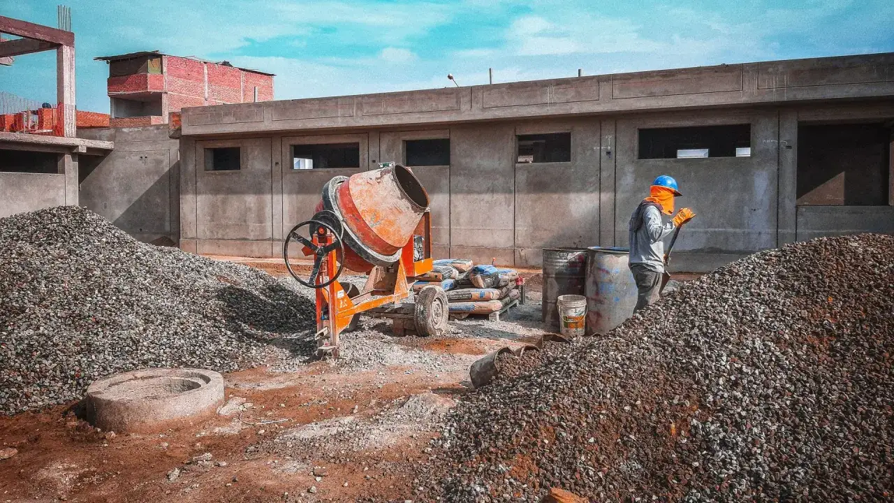 Chantier de construction avec b&eacute;tonni&egrave;re, sacs de ciment et ouvrier. Le dosage b&eacute;ton est essentiel pour la solidit&eacute;.
