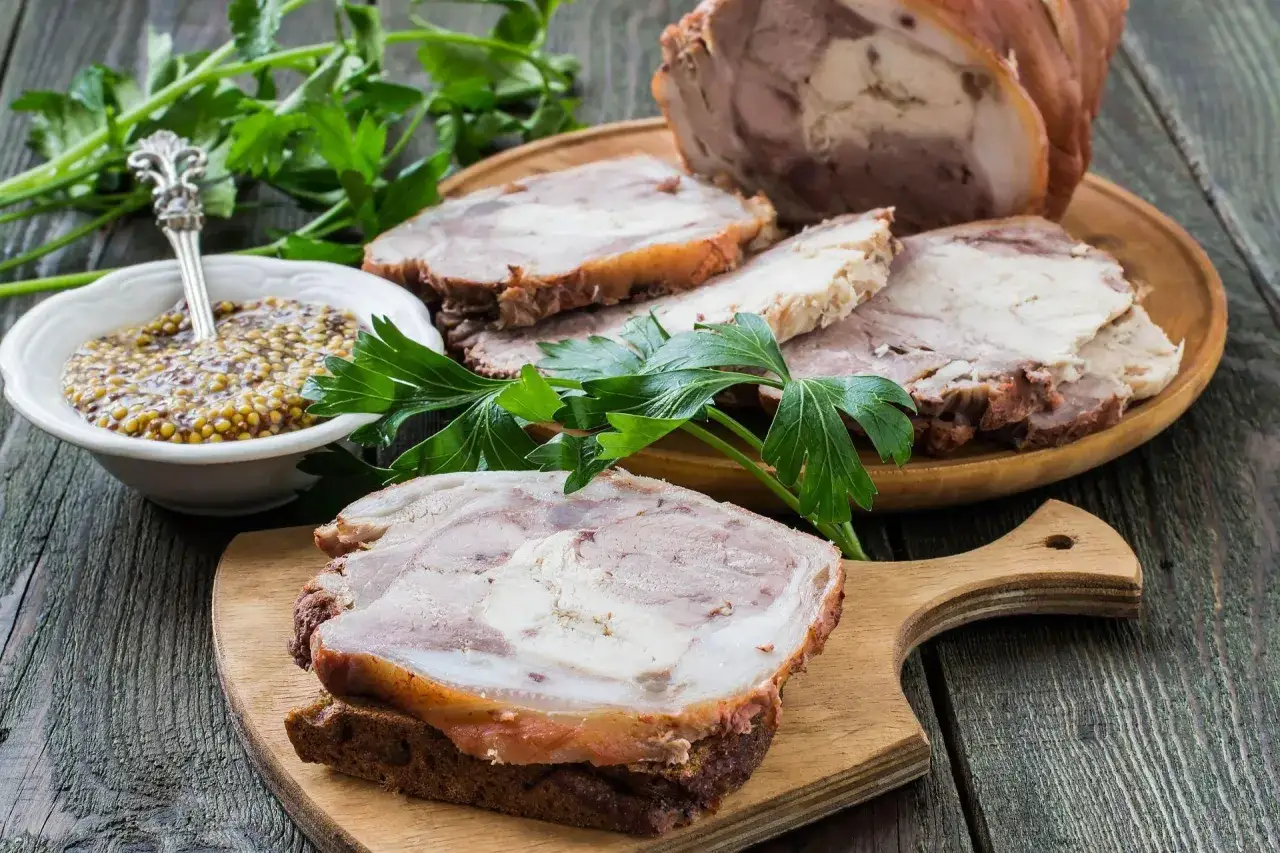 Domowy szynkowar: jak przygotować zdrowe wędliny z drobiu bez saletry. Pokrojona szynka z drobiu, musztarda ziarnista i natka pietruszki na drewnianym stole.