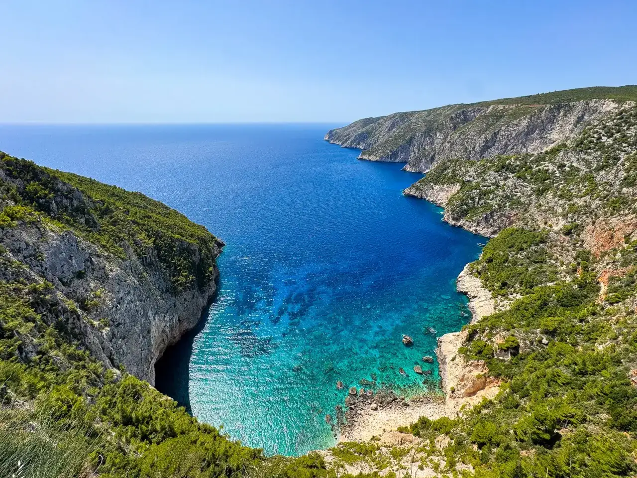 Widok na turkusową zatokę z klifami porośniętymi zielenią. Idealne miejsce na zakynthos wycieczki fakultatywne.