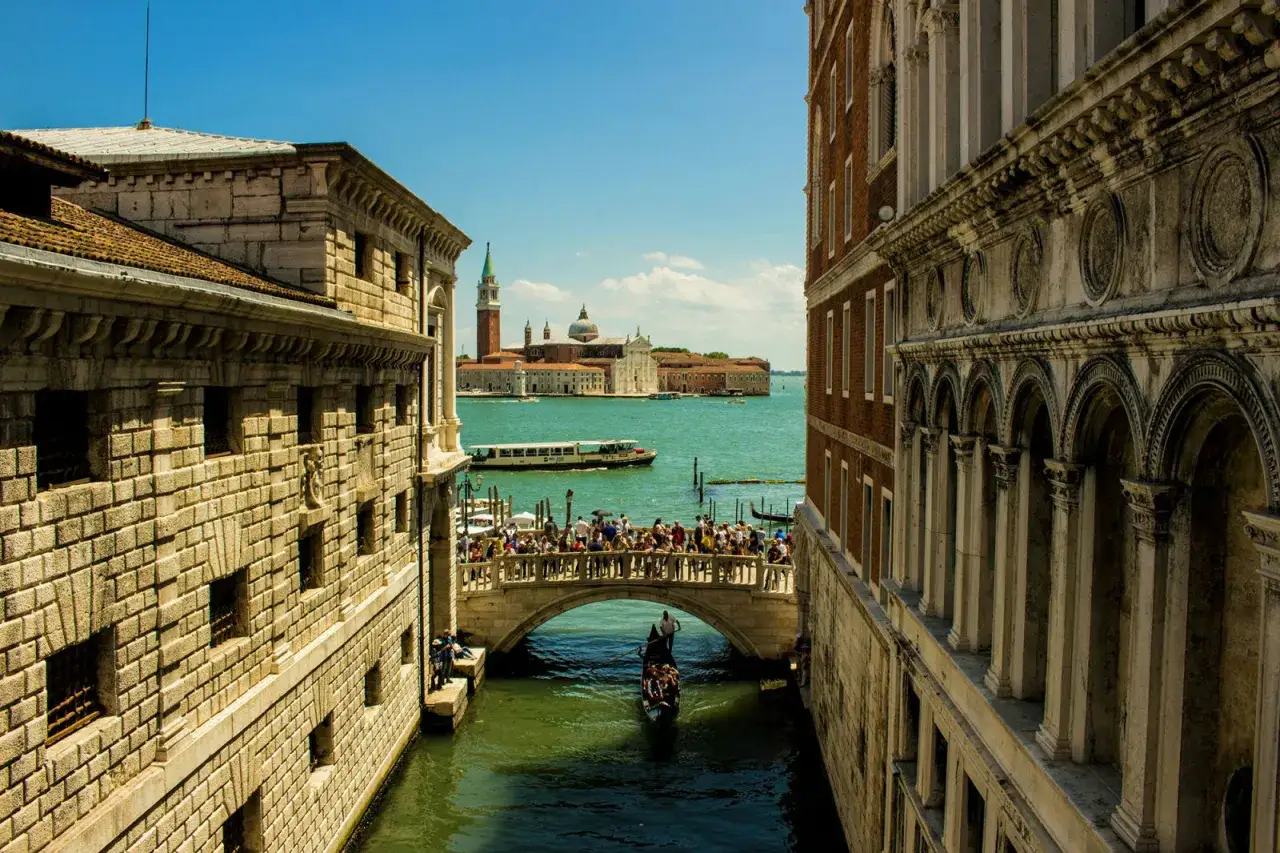 Un ponte di scorci a Venezia, con gondole e vaporetti, incorniciato da palazzi storici e la vista sull'isola di San Giorgio Maggiore.