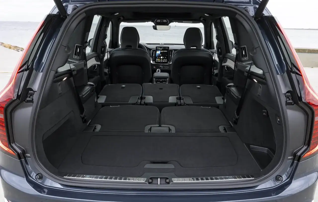 Wnętrze Volvo XC90 T8 z rozłożonymi siedzeniami, tworzącymi płaską przestrzeń bagażową. Widok na tylne siedzenia i deskę rozdzielczą.