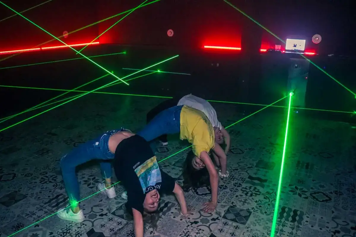 Chicas intentan pasar un **escape room Lacasitos** esquivando rayos láser verdes.