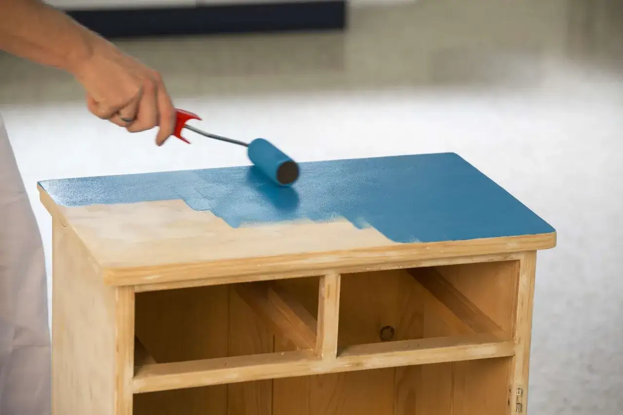 Hand rollt eine Kommode in leuchtendem Blau. Der Prozess, eine Kommode zu lackieren, verwandelt das Holzm&ouml;belst&uuml;ck.