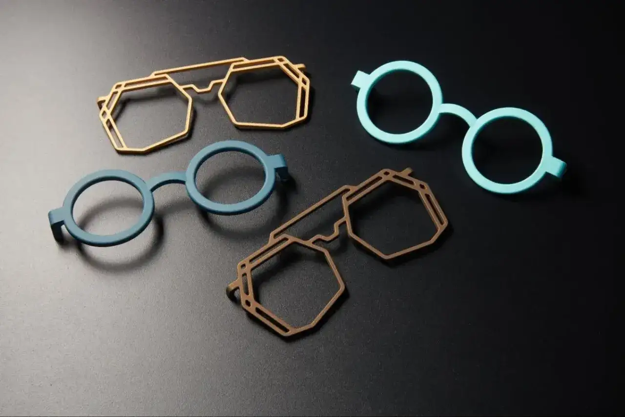 Four colorful 3d printing glasses frames in geometric and round styles are displayed on a black surface.