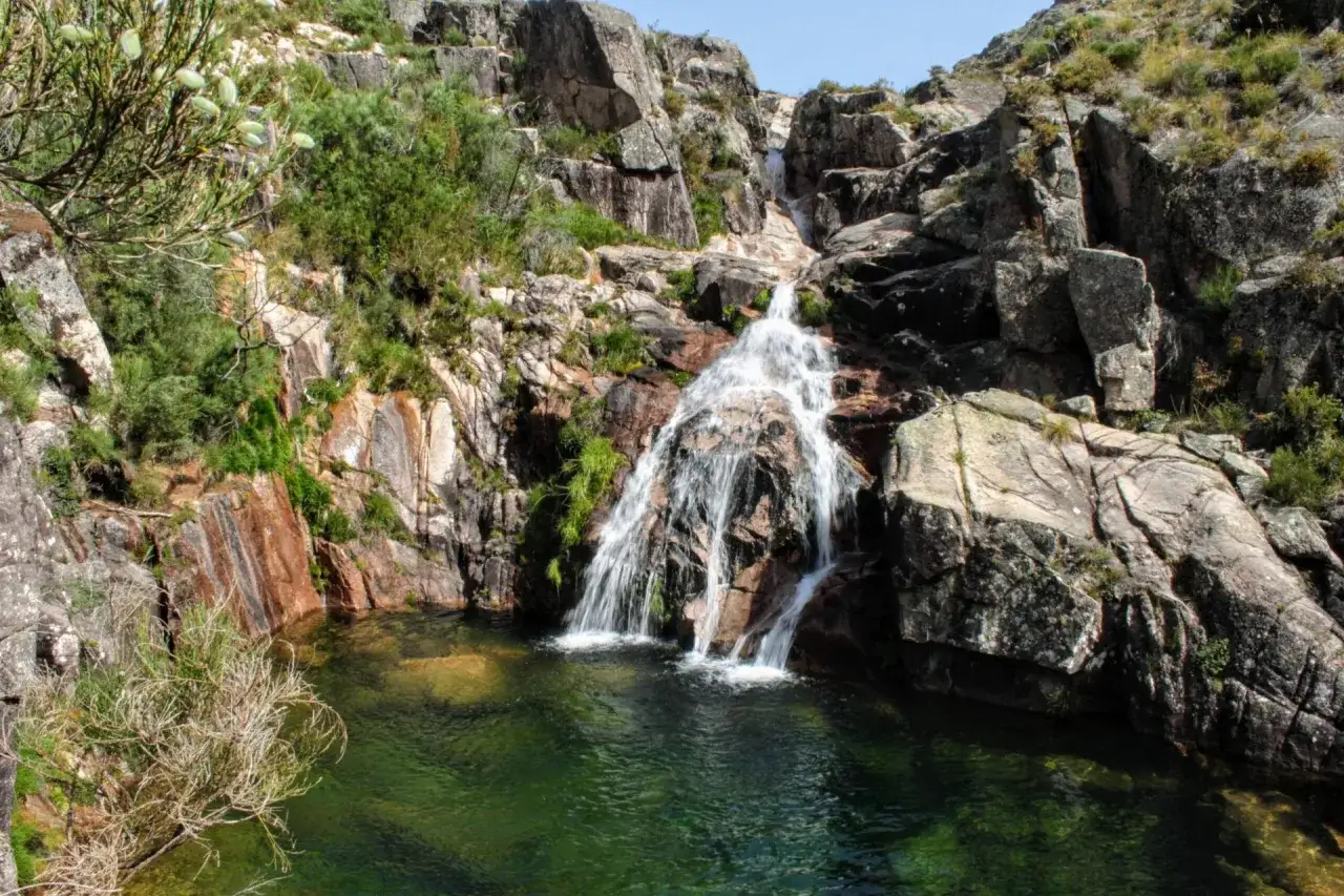 Ein Wasserfall st&uuml;rzt in ein smaragdgr&uuml;nes Becken. Felsen und &uuml;ppige Vegetation pr&auml;gen diese wilde portugiesische Natur.