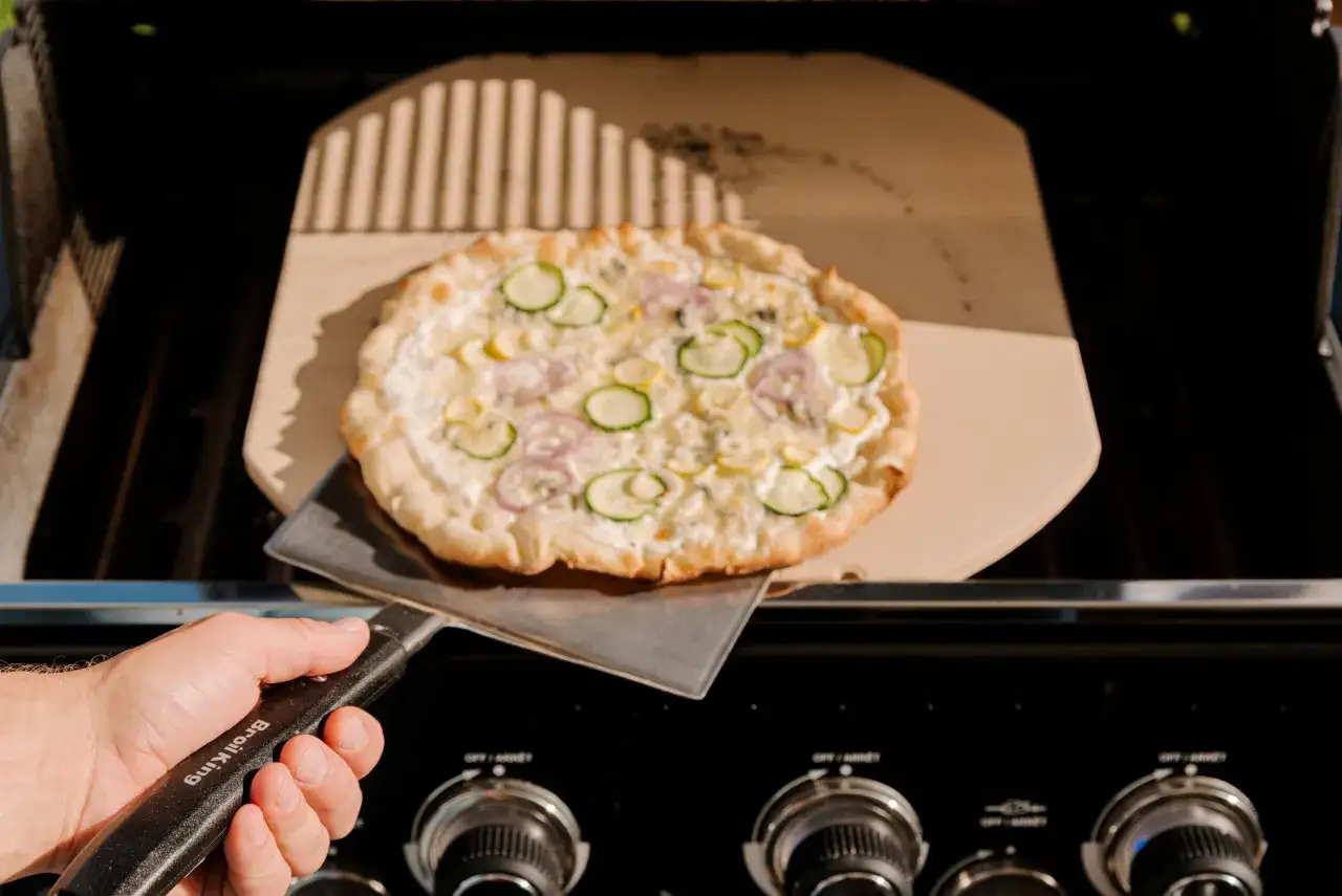 Pizza bianca z cukinią i cebulą na kamieniu do pizzy, gotowa do wrzucenia na grilla.