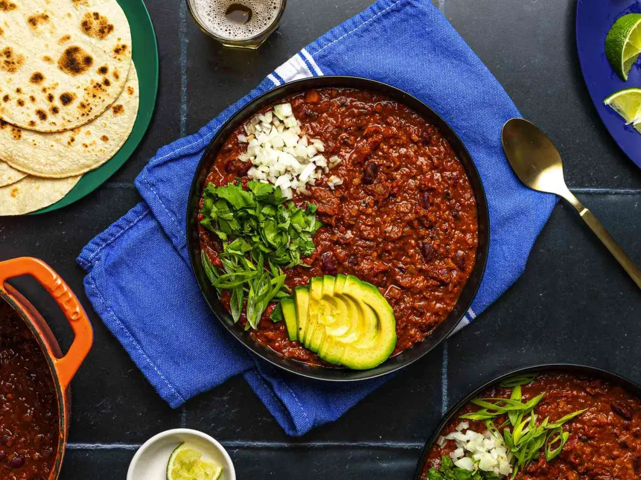 En skål med mustig chili sin carne, toppad med lök, koriander och avokado. Serveras med tortillabröd och lime.