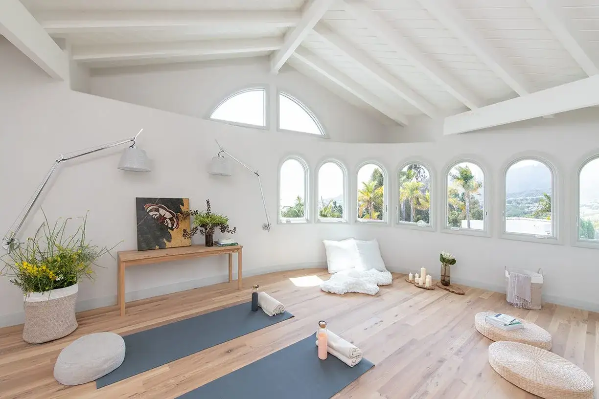 Ett ljust och luftigt yogarum hemma med två yogamattor, kuddar och en vacker utsikt genom välvda fönster.