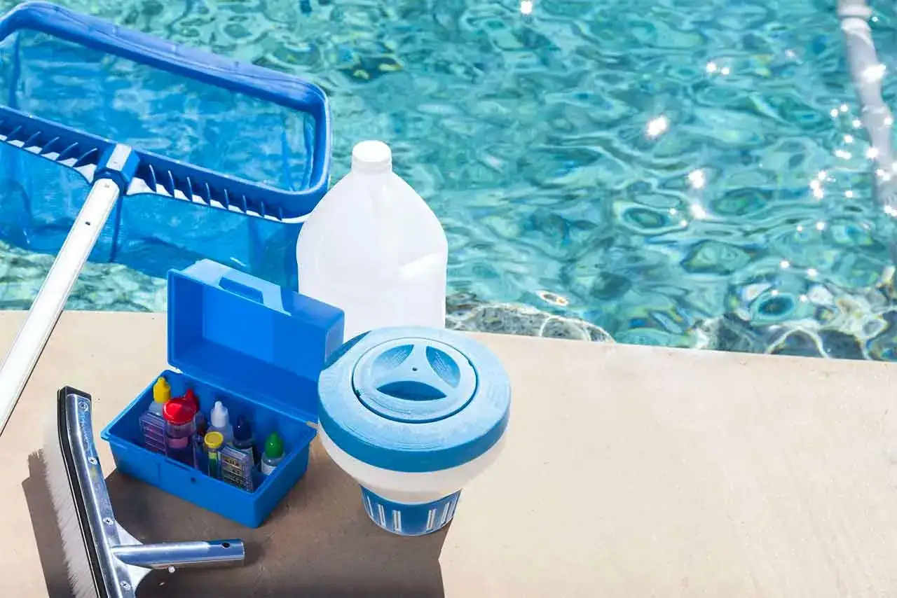 Pool cleaning supplies: net, brush, test kit, chlorine dispenser, and a large jug. Essential items for learning how to clean a pool filter and maintain clear water.