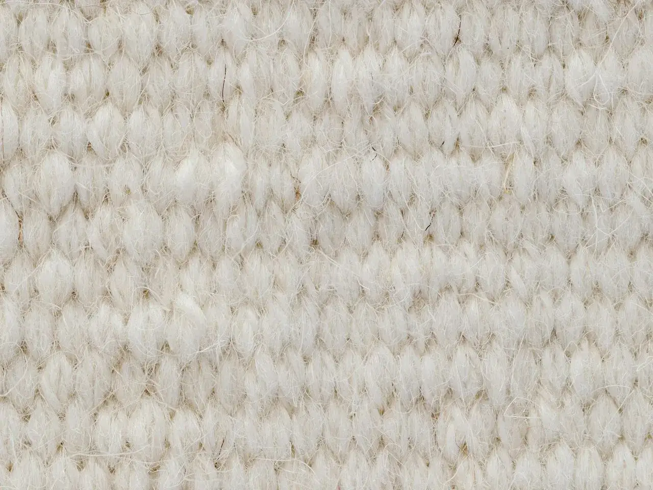 Zbliżenie na kremowy, tkany materiał. Delikatne włókna wełny merino tworzą gęsty, pleciony wzór, podkreślając jej naturalne właściwości.