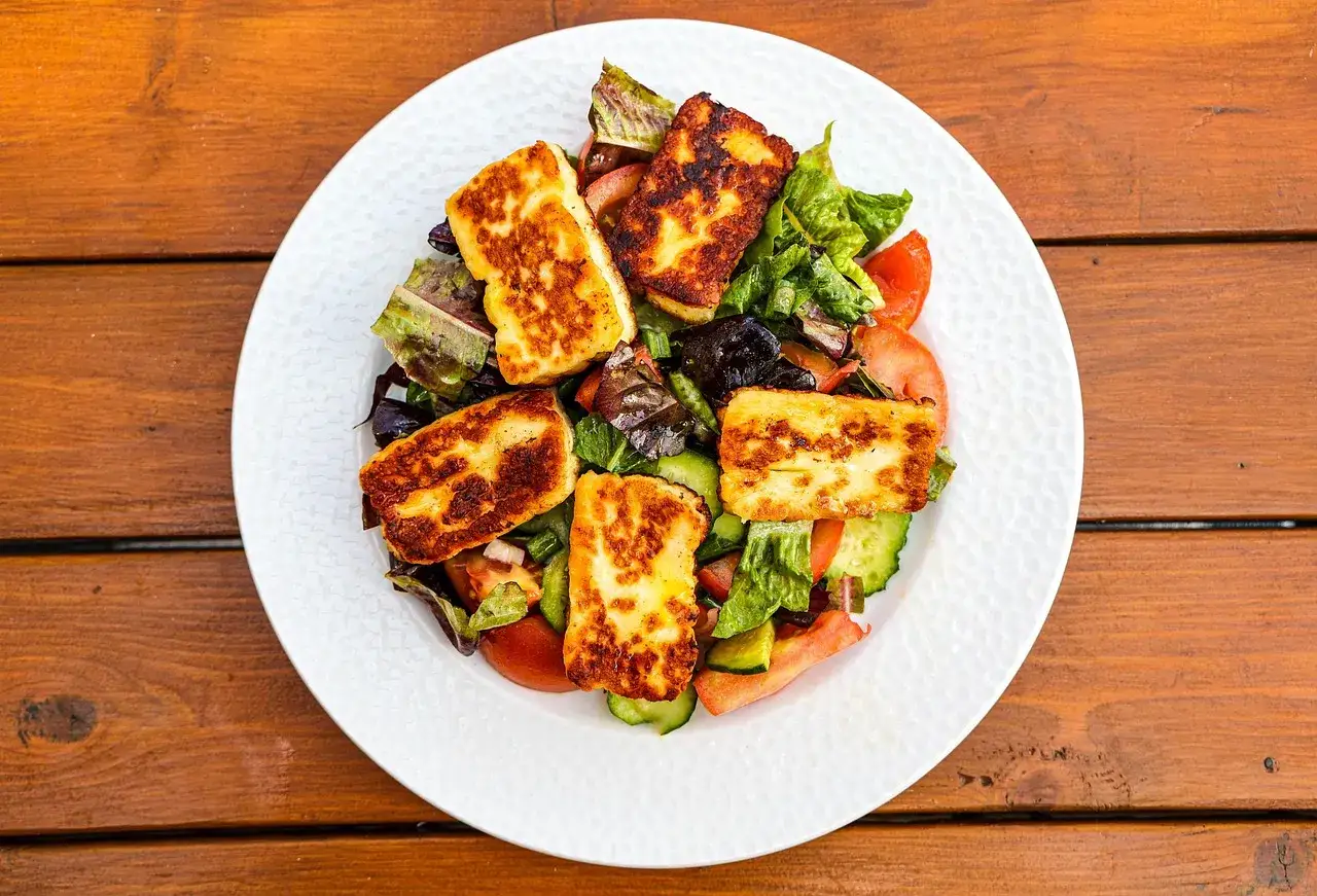 Sałatka z grillowanym serem halloumi, pomidorami i ogórkiem. Pyszny smak kuchni cypryjskiej na białym talerzu.