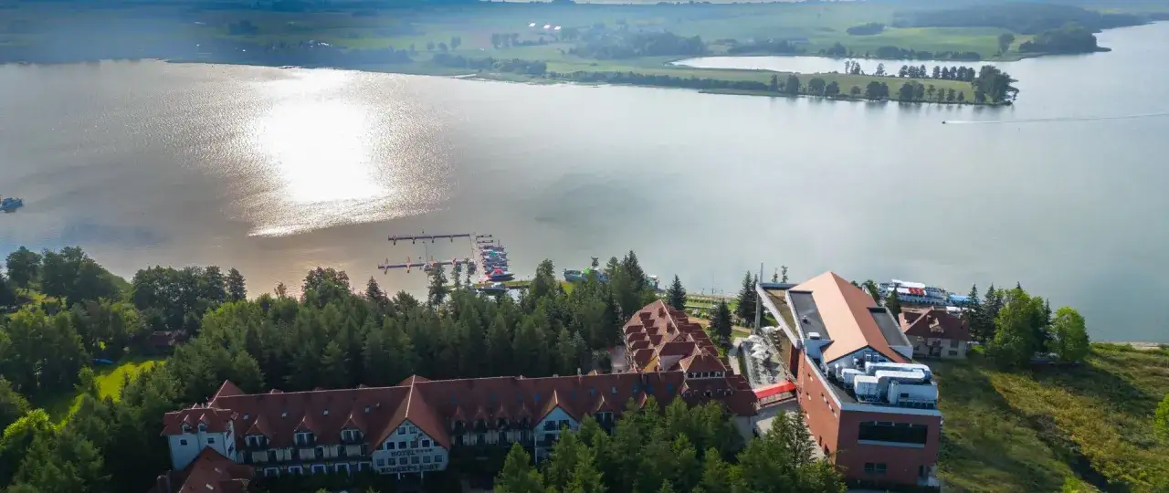 Malownicze konferencje na Mazurach: hotel Robert's Port nad jeziorem, z pomostem i łodziami.