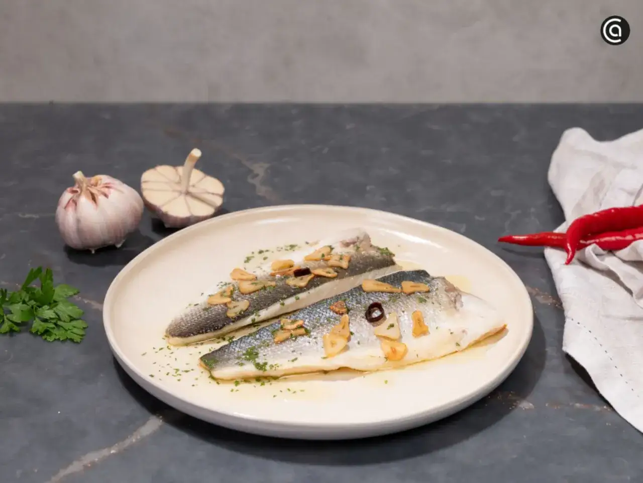 Dos filetes de lubina a la donostiarra, con l&aacute;minas de ajo dorado, perejil picado y un toque de guindilla.