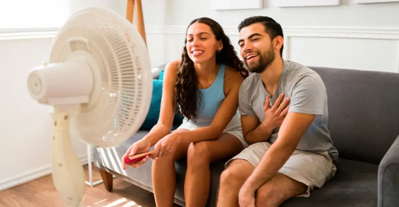 Pareja sonriendo y disfrutando del aire fresco de un ventilador en un d&iacute;a caluroso, sin aire acondicionado.