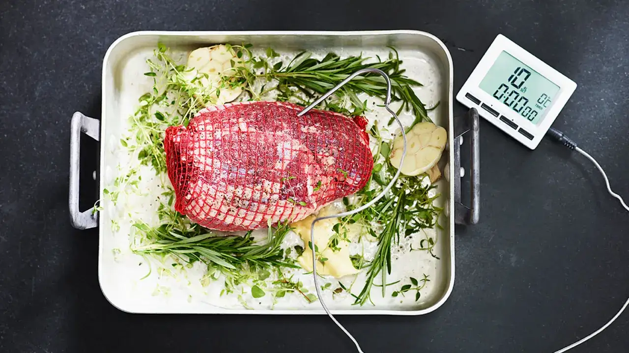 Rå entrecote i ugnsform med örter och vitlök, redo för ett perfekt entrecote recept. En digital termometer mäter temperaturen.