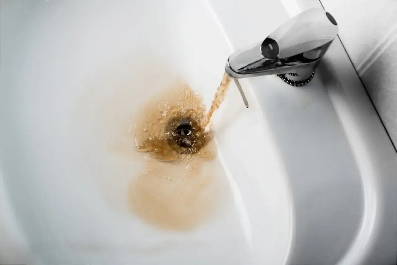 Acqua gialla dalla caldaia che scorre nel lavandino, creando un alone marrone.