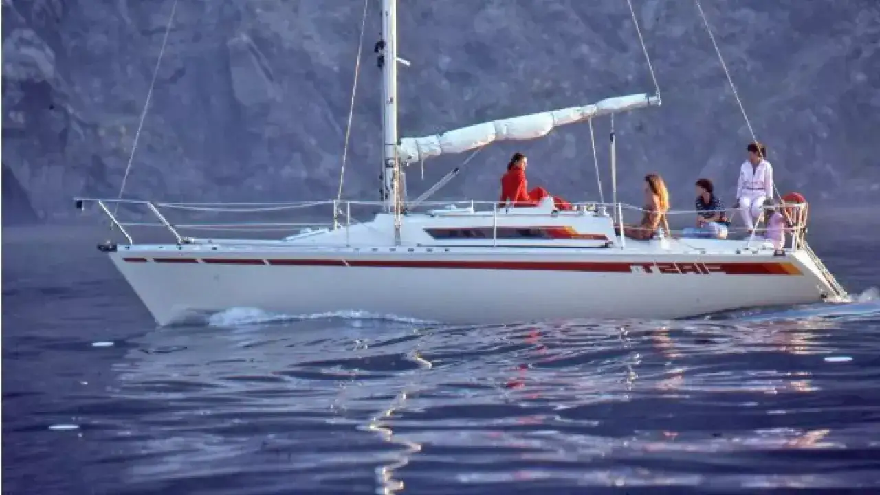 Voilier First 32 naviguant sur une eau calme, avec quatre personnes à bord profitant du soleil.