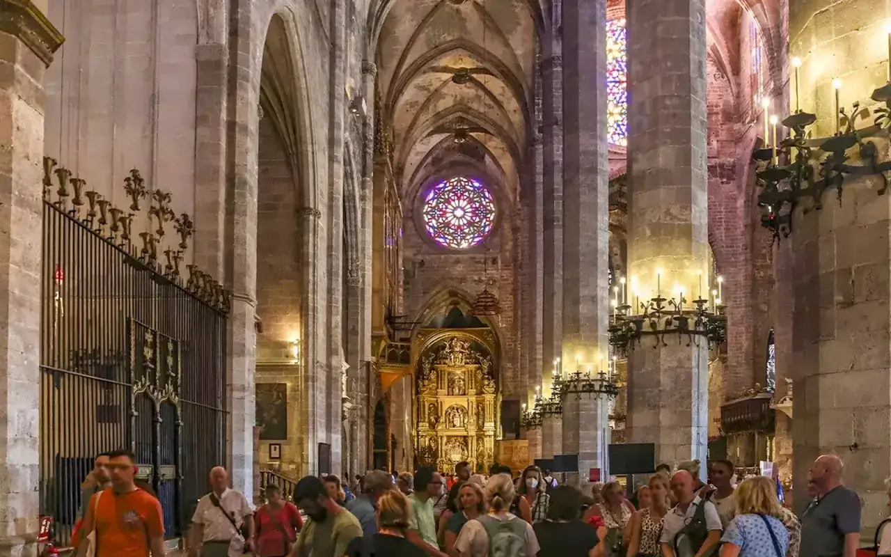 Bes&ouml;kare beundrar katedralens interi&ouml;r i Palma de Mallorca, med dess imponerande rosettf&ouml;nster och gyllene altare.