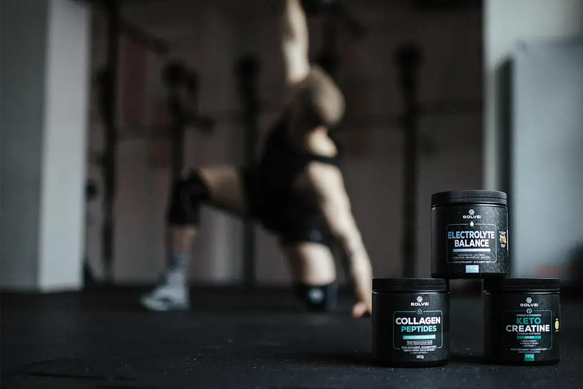Trzy odżywki: Electrolyte Balance, Collagen Peptides i Keto Creatine, idealne jako jakie odżywki na crossfit. W tle ćwiczący sportowiec.
