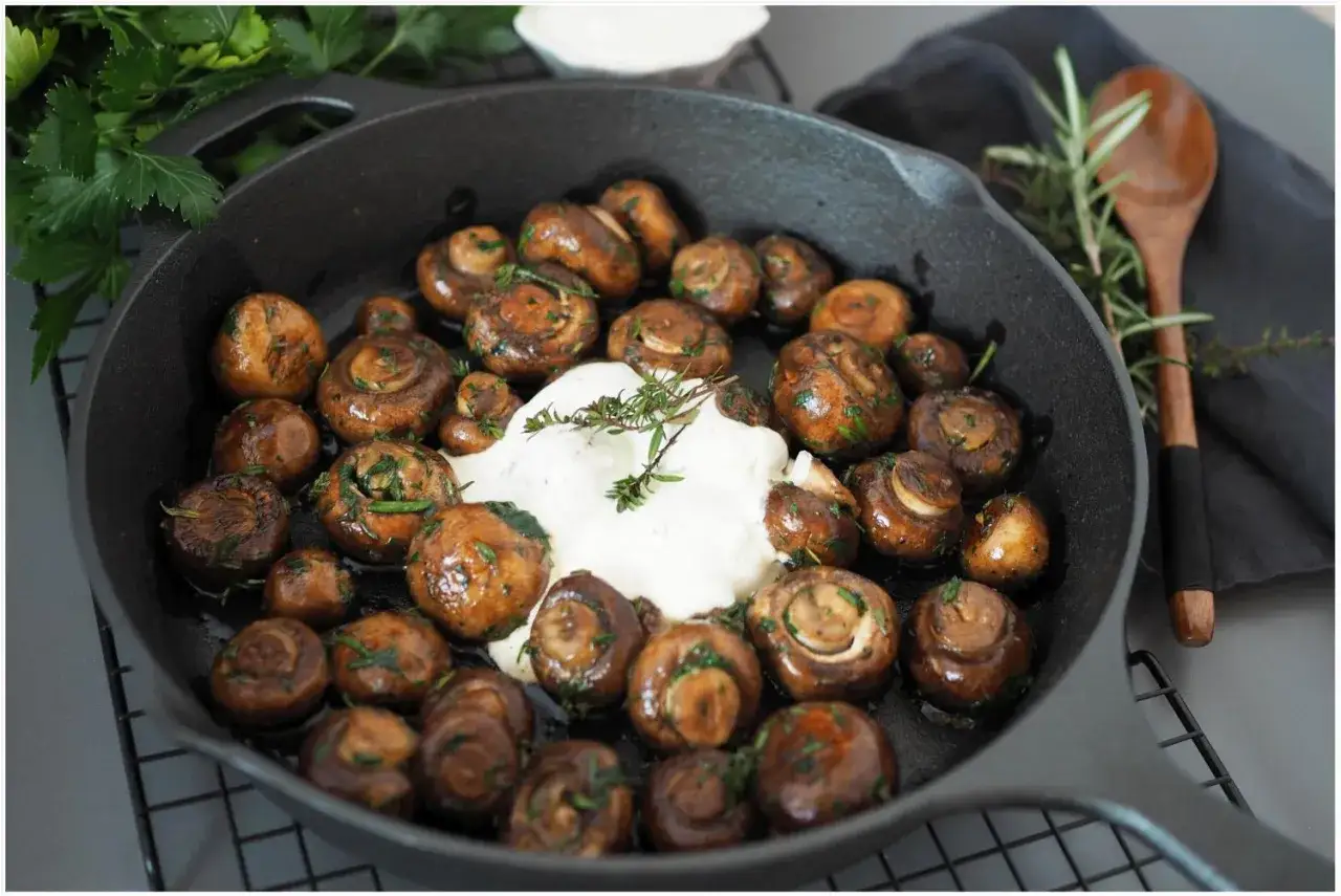Gebratene Champignons mit Kräutern in einer Gusseisenpfanne, serviert mit einer cremigen Sauce und garniert mit frischem Thymian.