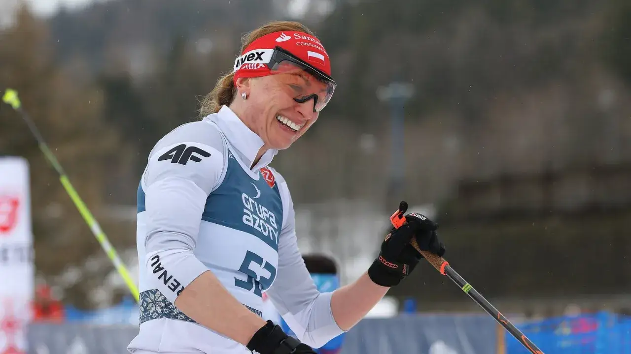 Uśmiechnięta Justyna Kowalczyk, mimo trudności z depresją, triumfuje na trasie narciarskiej.