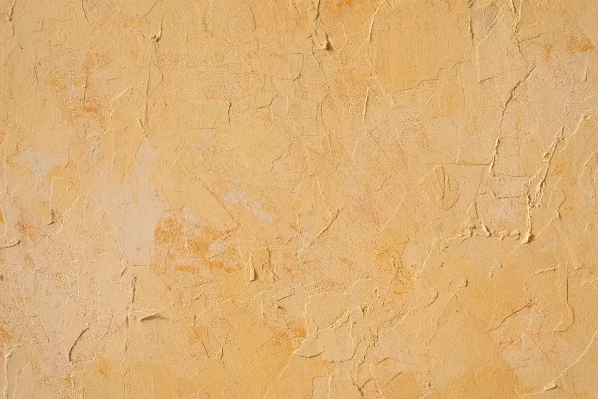Texture d'un mur avec un enduit taloch&eacute; ou gratt&eacute;, aux nuances chaudes de jaune et d'ocre, &eacute;voquant un style rustique et chaleureux.