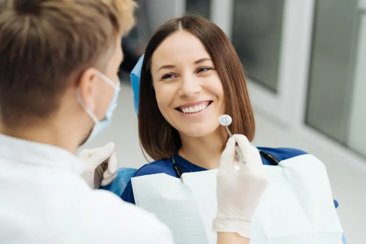 Uśmiechnięta pacjentka u dentysty, która pokonała dentofobię. Lekarz w masce i rękawiczkach bada jej zęby.