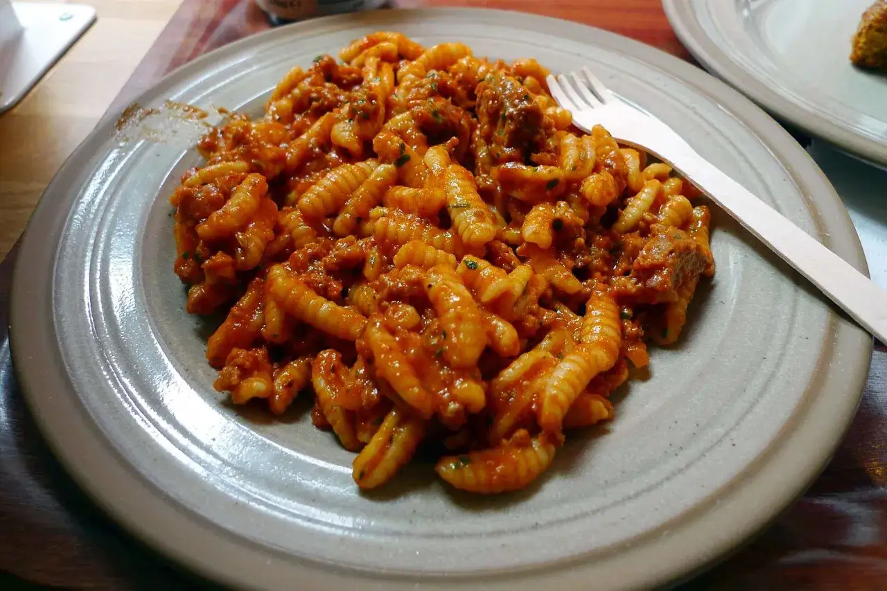 Un piatto di gnocchetti alla campidanese, conditi con un ricco sugo di pomodoro e carne, pronti per essere gustati con una forchetta di legno.