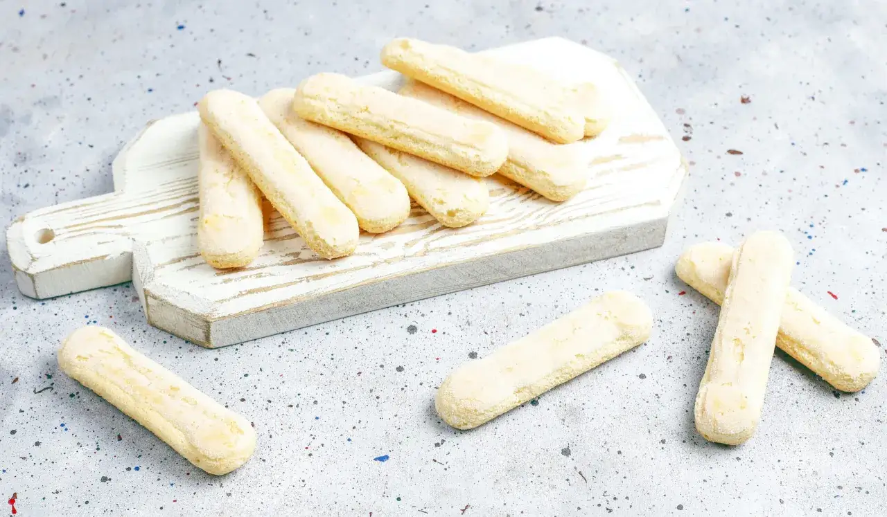 Savoiardi pronti per la ricetta del tiramis&ugrave;, disposti su un tagliere bianco.