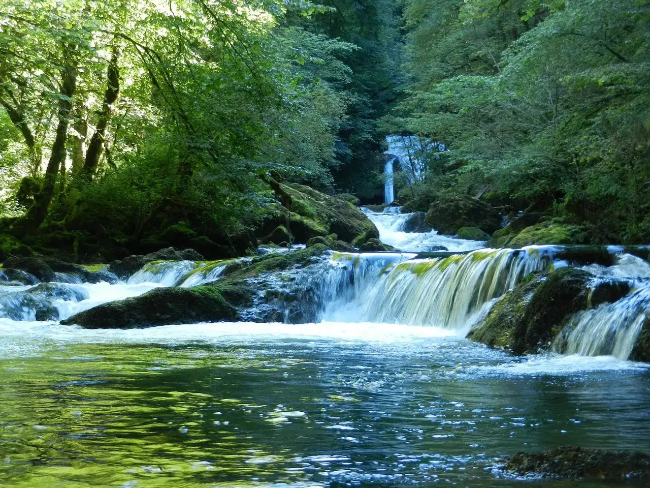 Cascades et forêt luxuriante, un aperçu de ce que visiter dans le Doubs. L'eau vive dévale les rochers moussus, invitant à la contemplation.