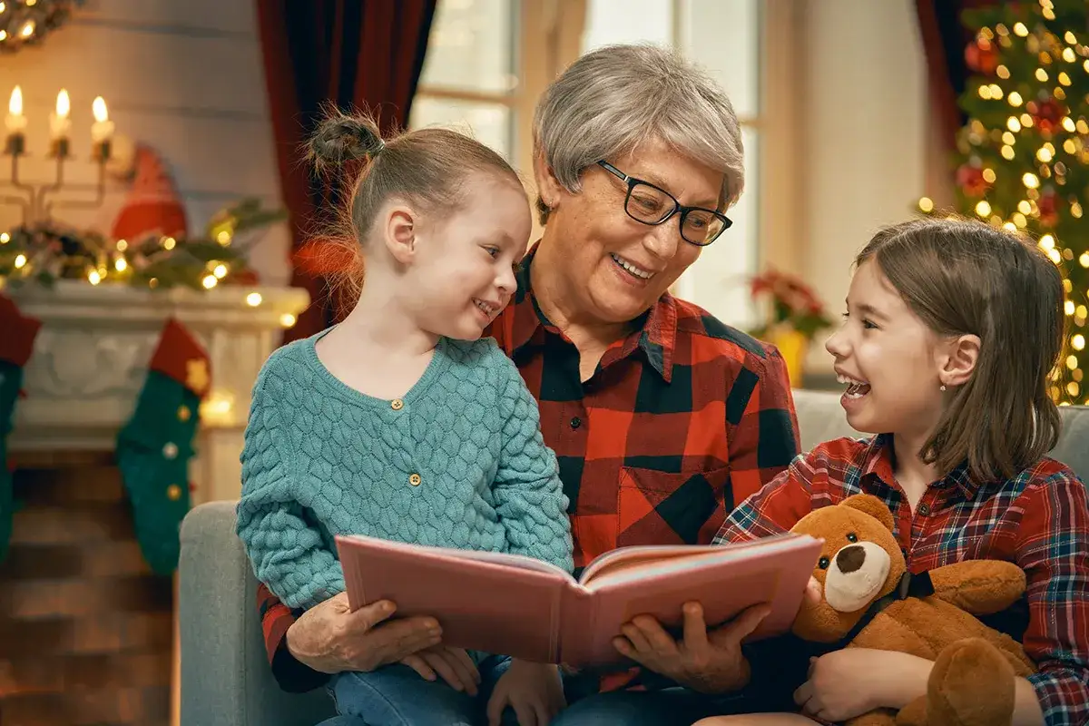 Abuela lee un cuento de Navidad a sus nietas junto al &aacute;rbol.