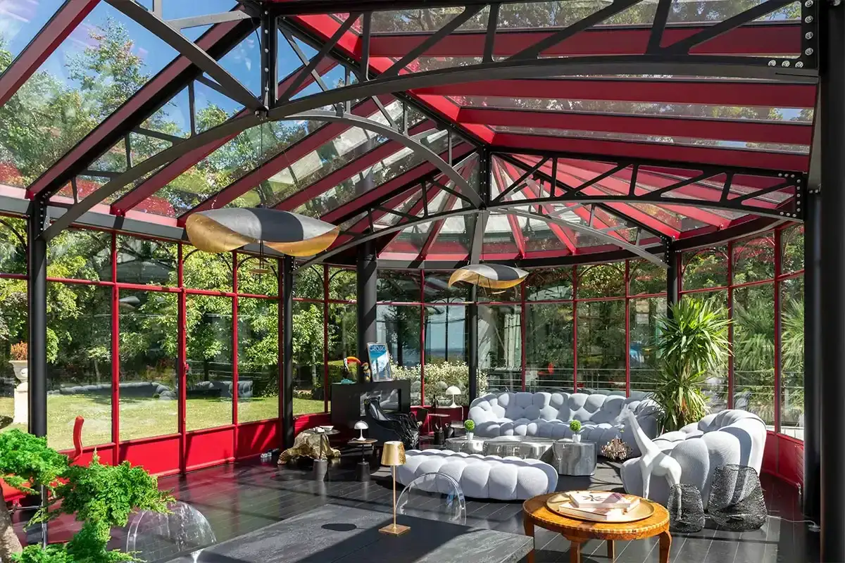 Int&eacute;rieur d'une **veranda en fer forg&eacute;** aux couleurs vives, avec des canap&eacute;s moelleux et une vue sur un jardin luxuriant.